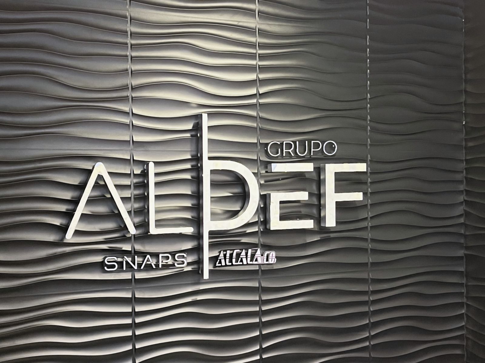Acercamiento al anuncio luminoso GRUPO ALDEF sobre muro de paneles ondulados negros