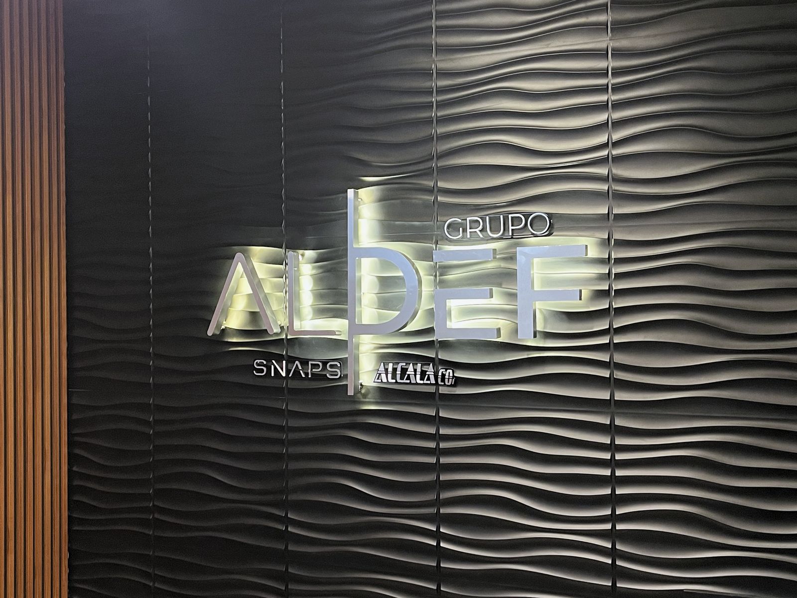 Vista en perspectiva del anuncio luminoso GRUPO ALDEF junto a un muro de madera