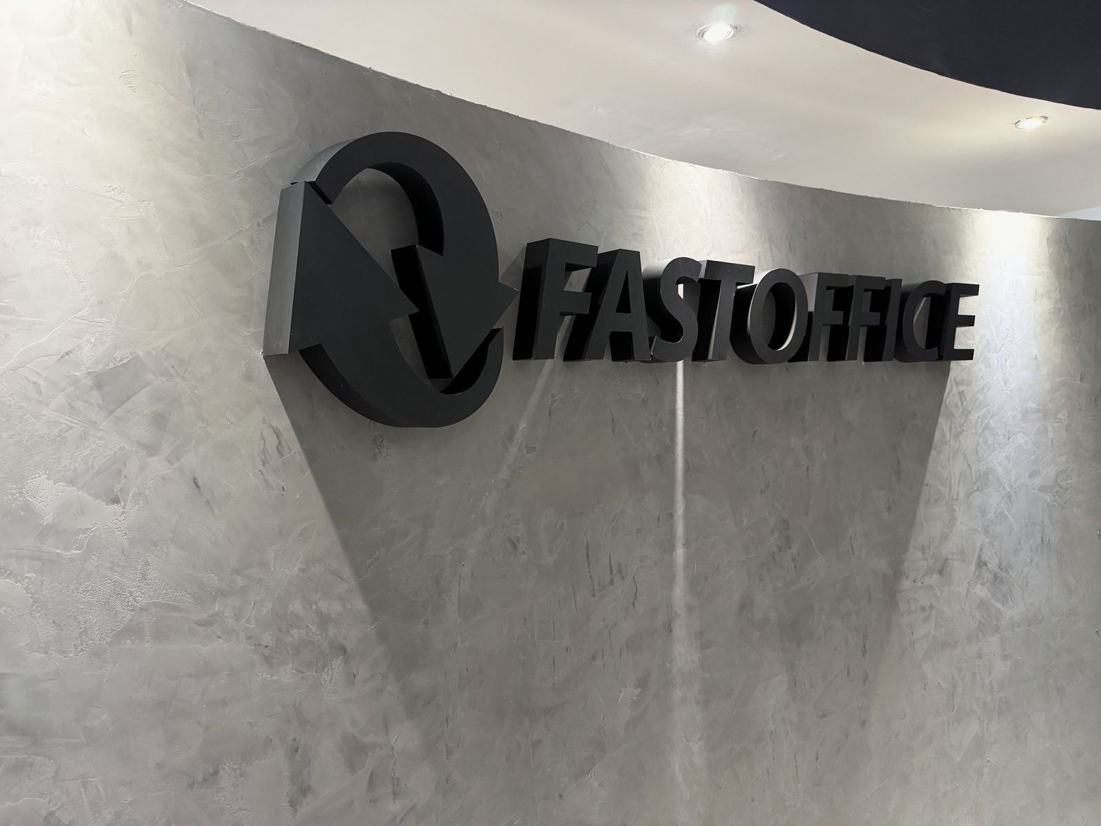 Anuncio FASTOFFICE en letras y logotipo de aluminio pintado en negro mate sobre muro de textura gris