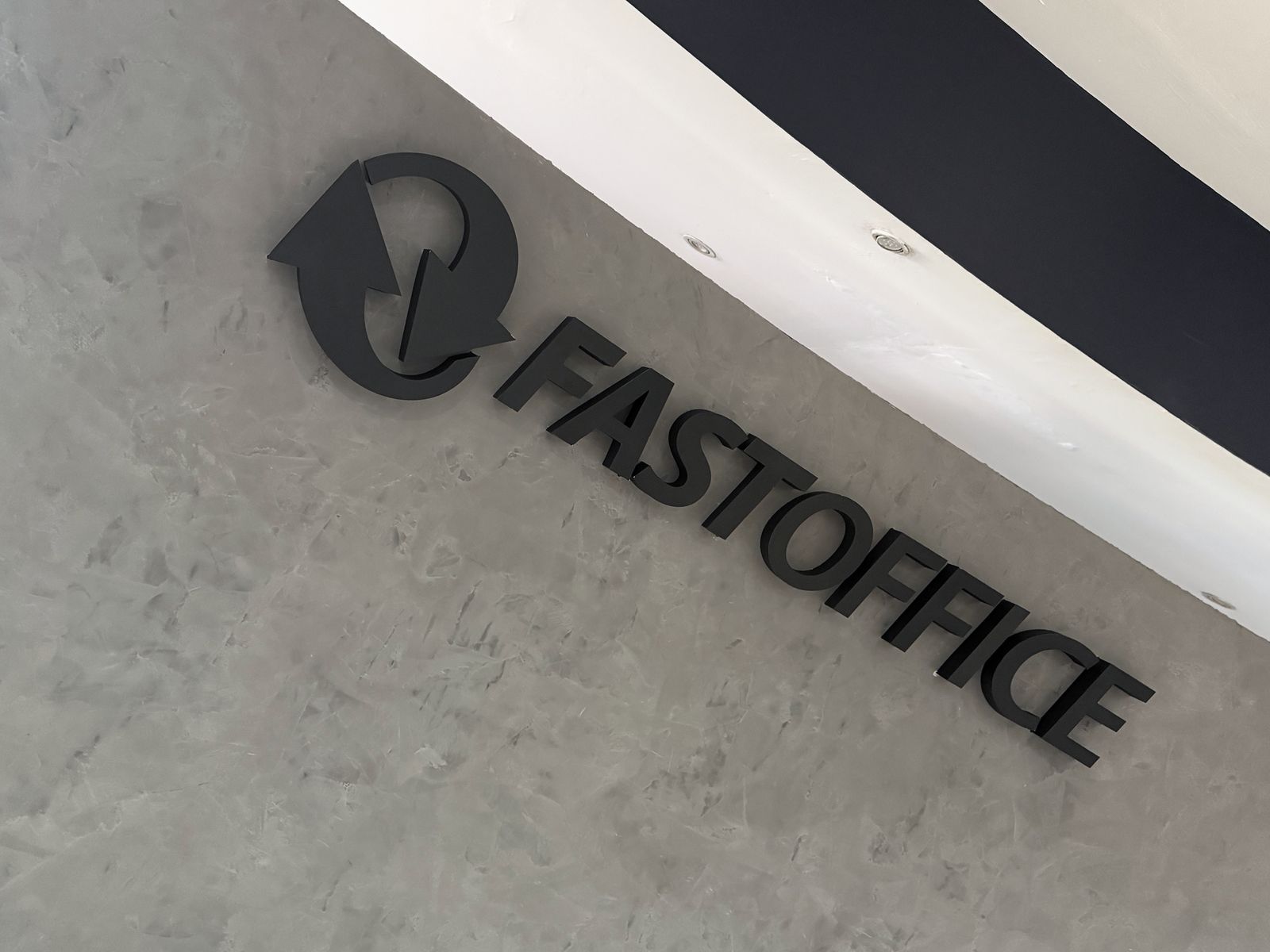 Detalle en perspectiva del logotipo y las letras FASTOFFICE en aluminio negro mate