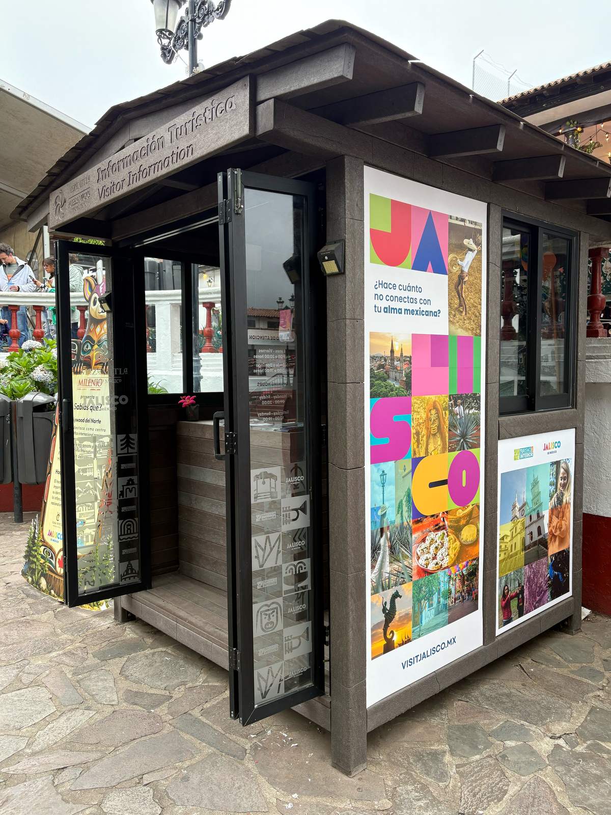 Kiosco de información turística en una plaza, con el gráfico JALISCO en letras de colores y fotos de destinos del estado
