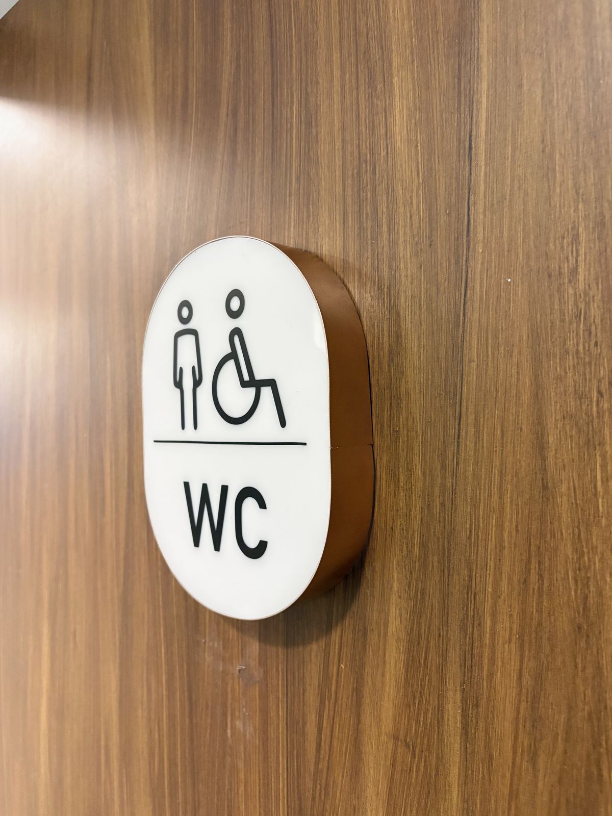 Letrero de sanitario WC con pictogramas de accesibilidad, montado sobre muro de madera