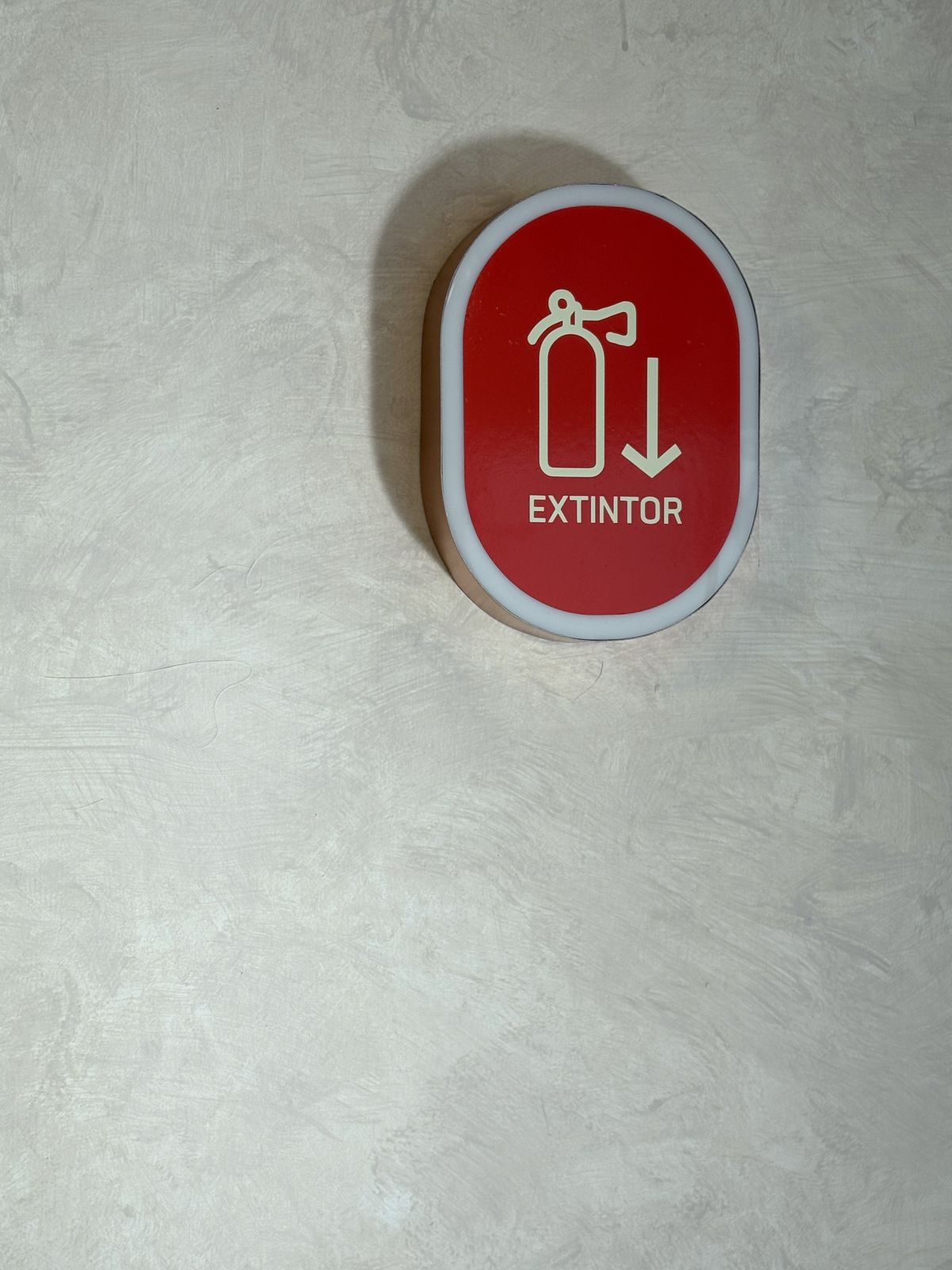 Letrero de extintor en rojo montado sobre muro de textura clara
